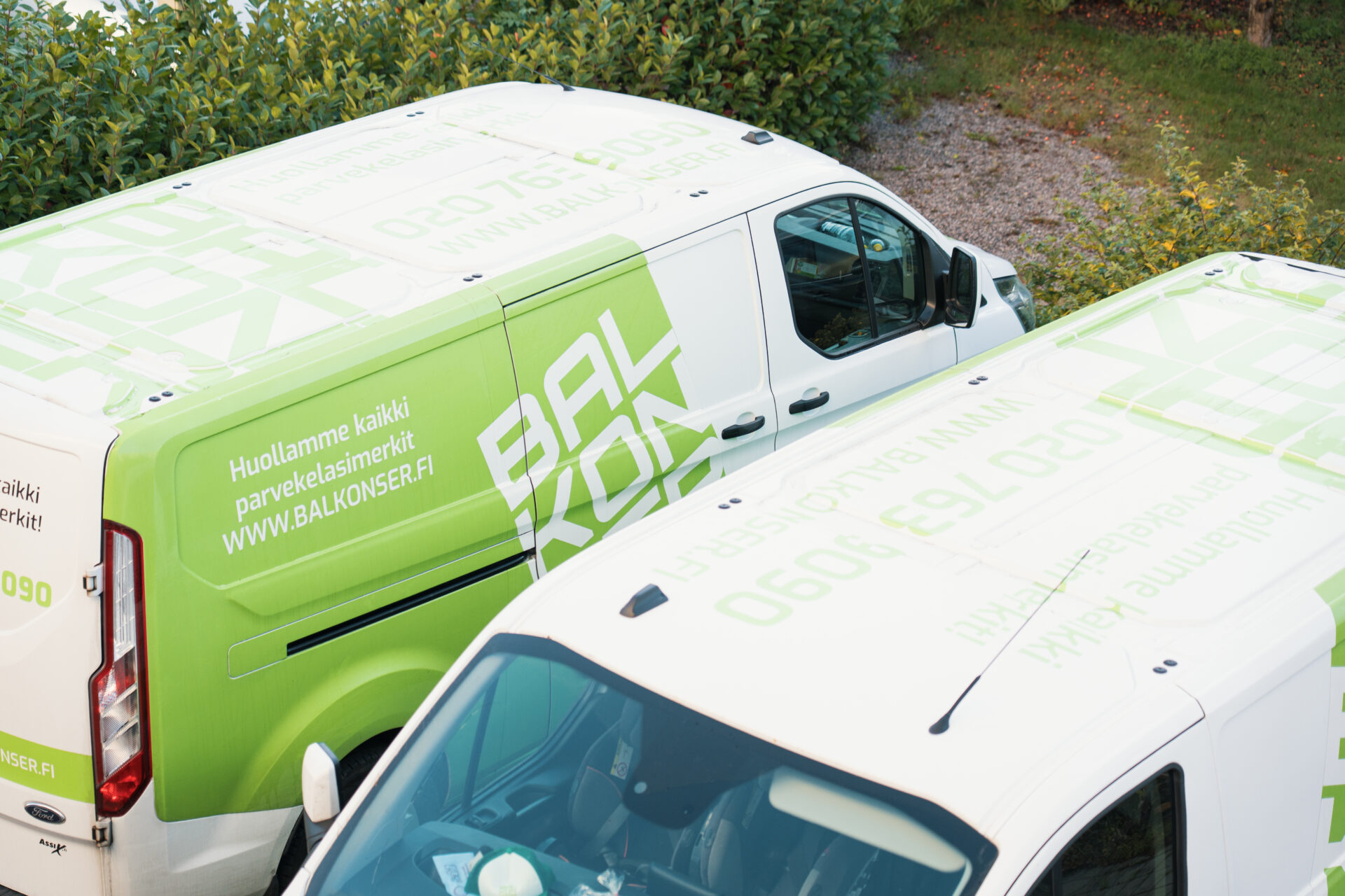 Kaksi vihreä-valkoista Balkonserin huoltoautoa pysäköitynä vierekkäin.